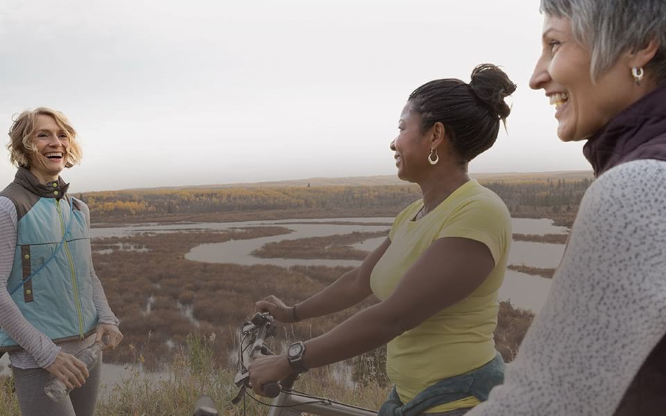 Women of all ages exercising on bikes and hiking through a marsh
