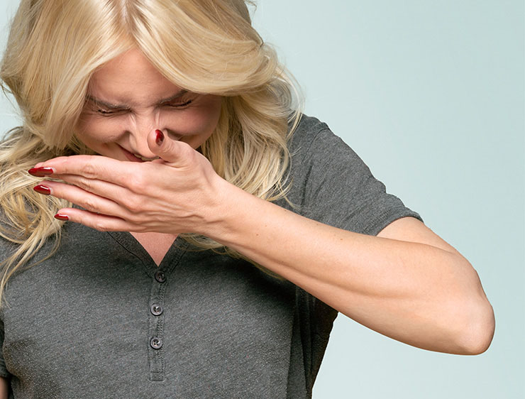 Woman sneezes into hand.